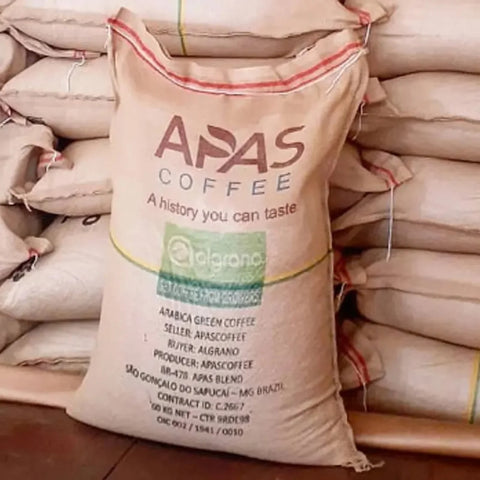 Jutesack mit dem Aufdruck Apas Coffee, gefüllt mit Rohkaffee aus São Gonçalo do Sapucaí in Minas Gerais, vor weiteren gestapelten Säcken