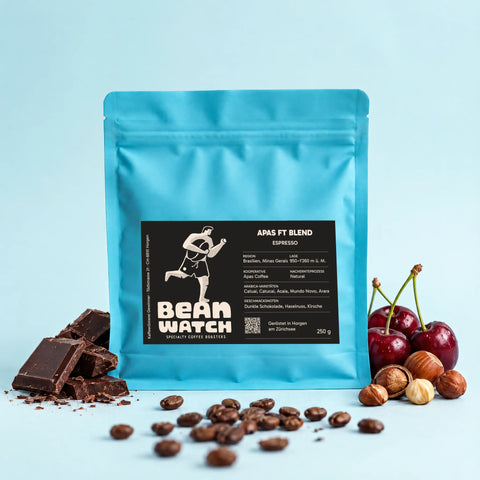 A bag of our Apas FT Blend Espresso against a blue studio background with dark chocolate, hazelnuts, cherries and a few roasted coffee beans