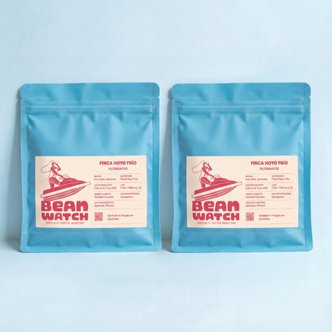 Zwei Beanwatch Finca Hoyo Frío Filterkaffees, türkise Kaffeepackungen mit pinker Schrift auf hellorangenem Etikett, aus unserer Dragonfruit Pink Linie
