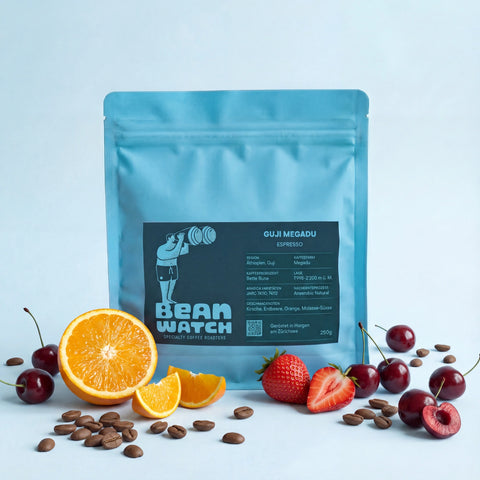 Ein Beutel Guji Megadu Espresso von Espresso, präsentiert vor Orangen Erdbeeren und Kirschen,die die Geschmacksaromen repräsentieren und einzelnen Kaffeebohnen, alles zusammen im Studio von Beanwatch