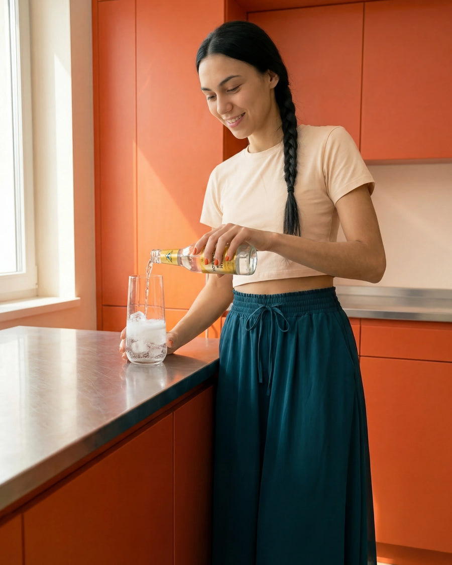 Julia giesst Tonic Water aus einer kleinen Flasche über Eiswürfel in ein hohes Glas und zeigt so den ersten Schritt zum Espresso Tonic.